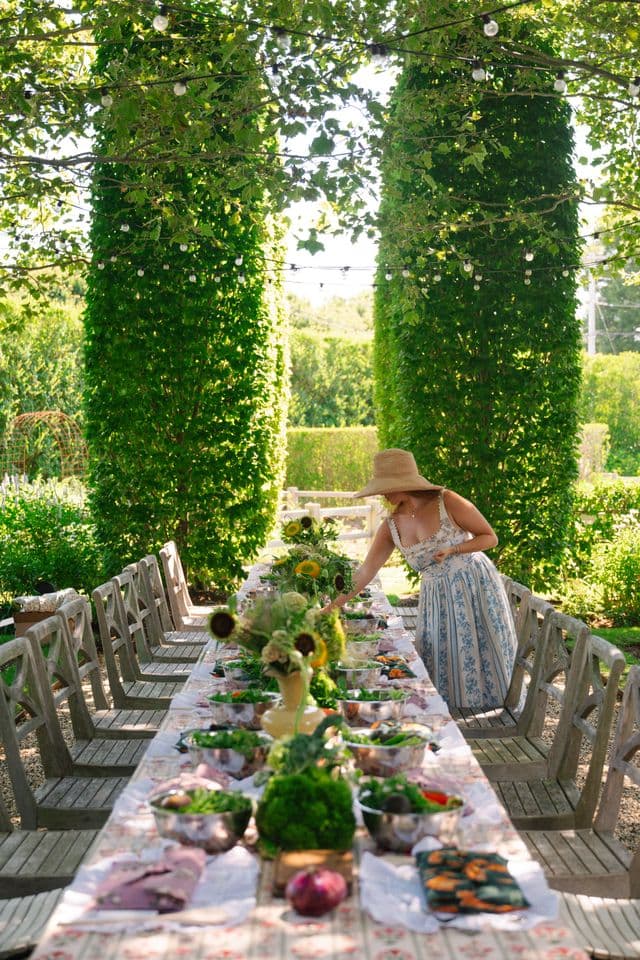 An event stylist finishing a long banquet table in a garden before guests arrive
