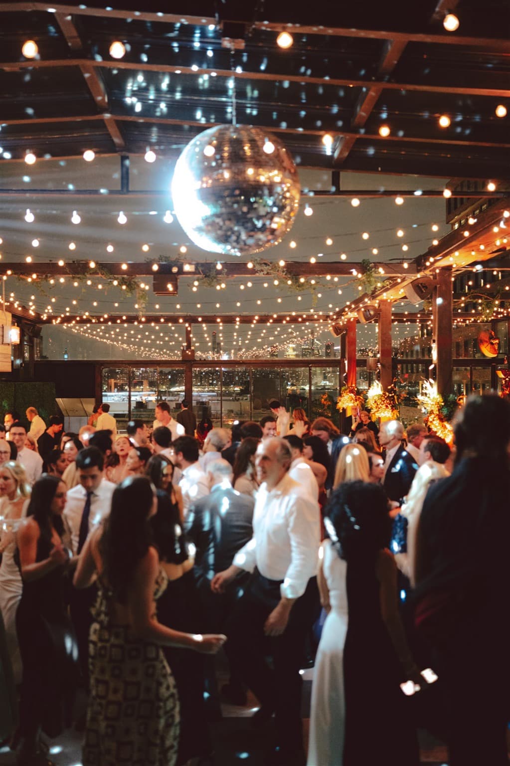 A rooftop dance floor under a mirror ball and canopies of string lights
