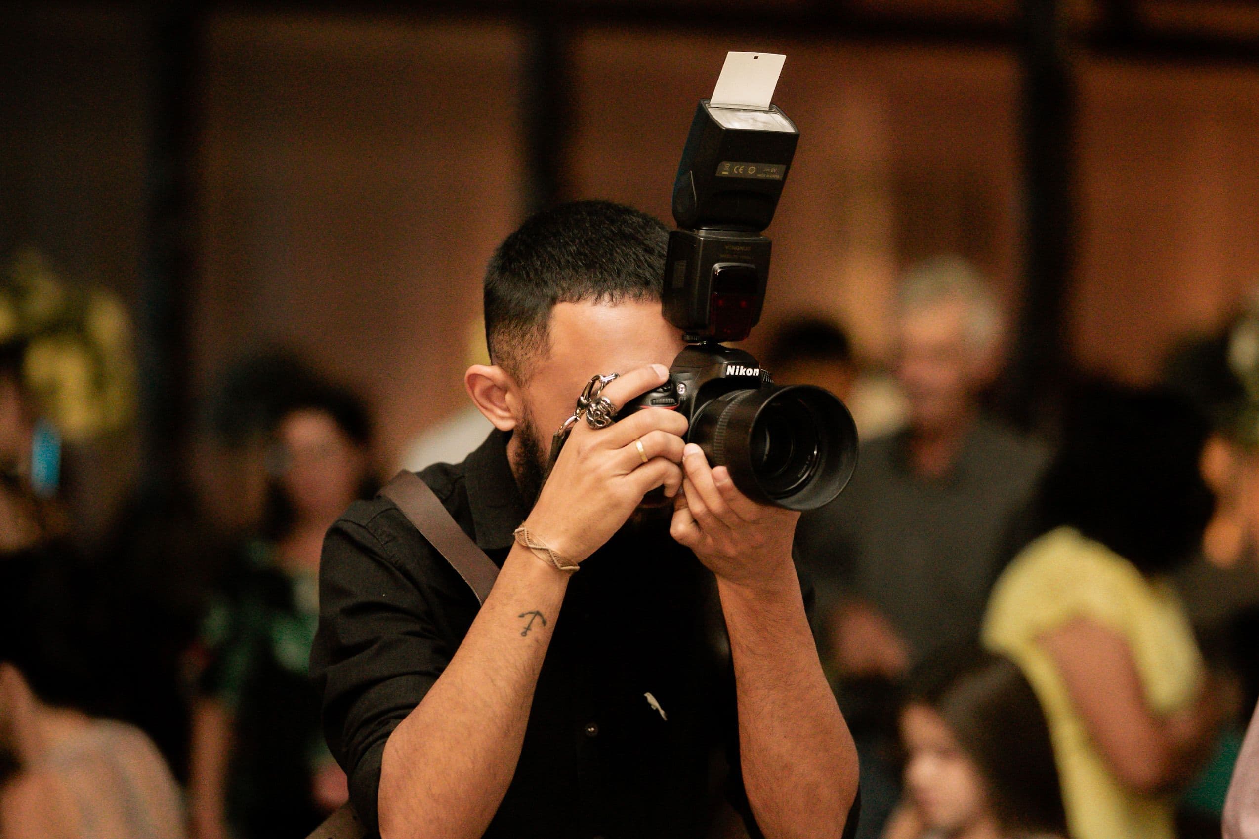 A photographer shooting with a flash-mounted DSLR in a crowded event room