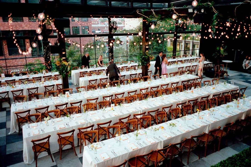 A rooftop reception styled with long banquet tables under strings of café lights