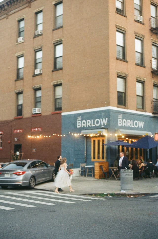 A corner venue strung with lights, guests arriving on the street outside